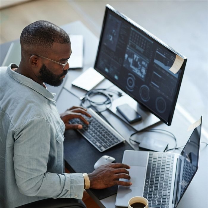 Developer working across a monitor and laptop with coffee in hand